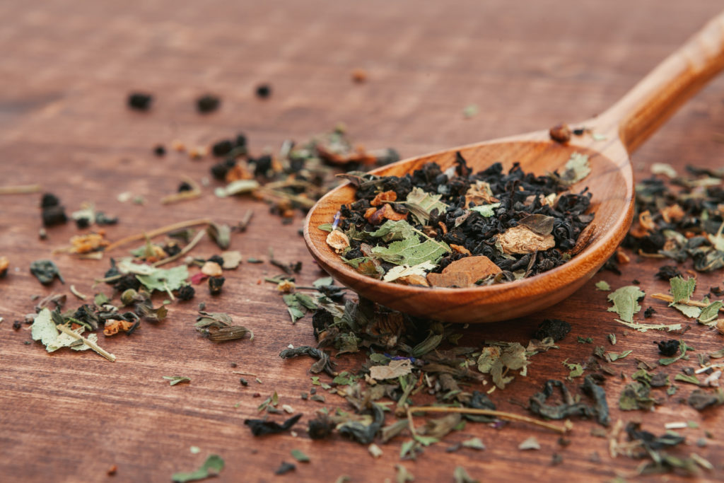 Black tea with herbs in wooden spoons on a wooden board