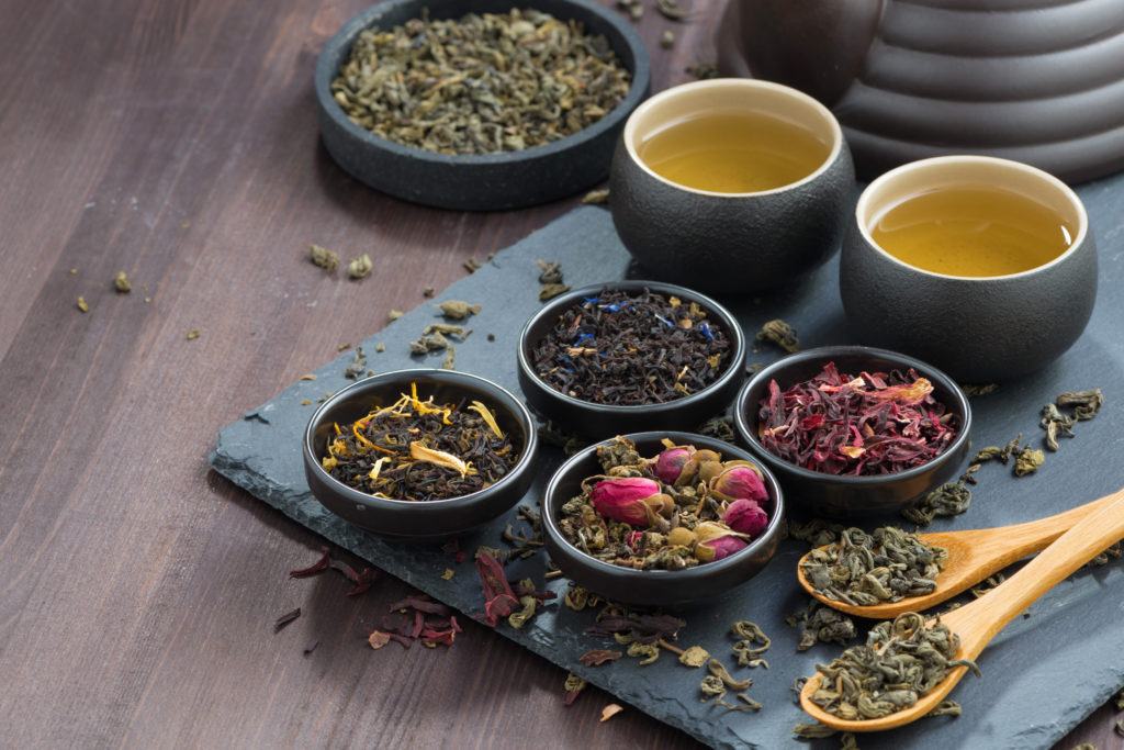 assortment of fragrant dried teas and green tea on wooden table, horizontal, close-up