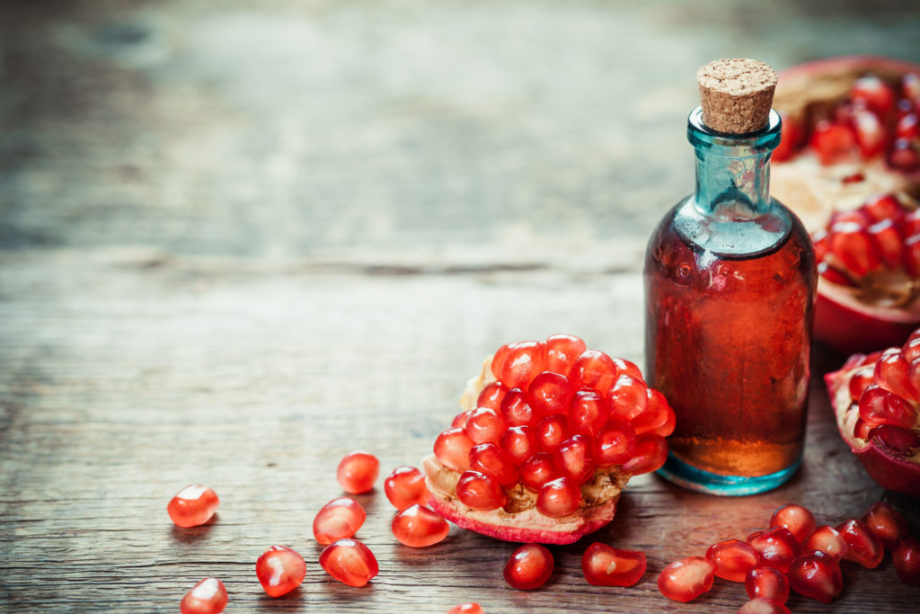 Pomegranate tincture or  juice and red ripe garnet fruit with seeds on wooden table. Selective focus.