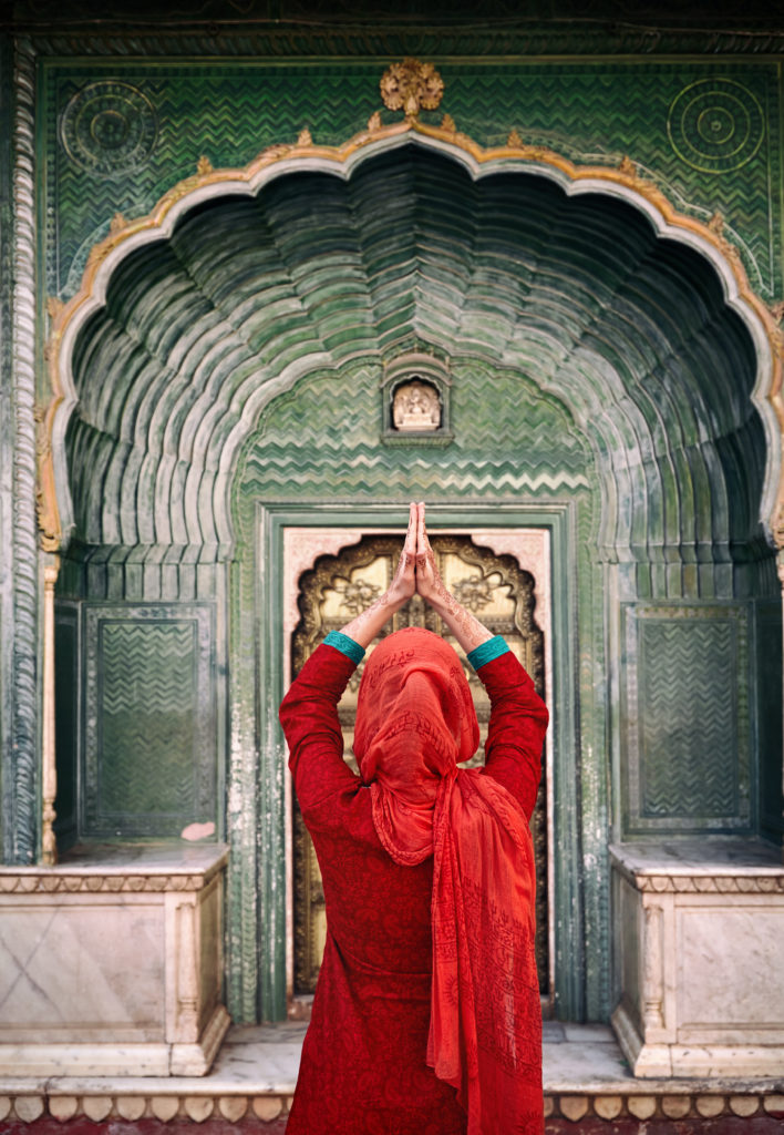 Indian Woman in red scarf with hands in prayer gesture at green gate door in City Palace of Jaipur, 
Rajasthan, India. Space for your text, can be used as book or magazine cover.